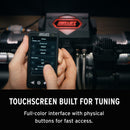 Hand holding a touchscreen device with a blurred background of vehicle air suspension equipment, featuring the brand Air Lift Performance